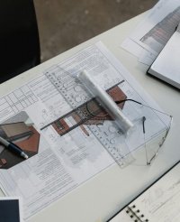 Architect sketching floor plan lines on tracing paper with technical tools, representing the precision and craft behind professional 2D plans.